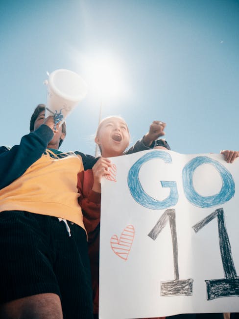 Group of enthusiastic people cheering outdoors, holding a sign with 'GO 11' under bright daylight. 
