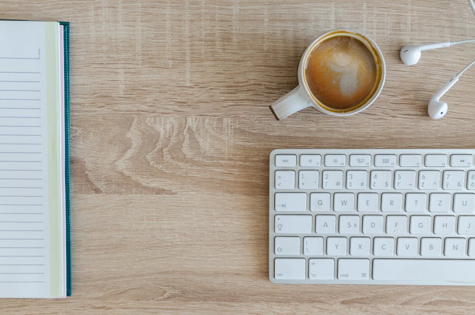 Flat lay of a workspace featuring coffee, a keyboard, and a notebook on a wooden desk.