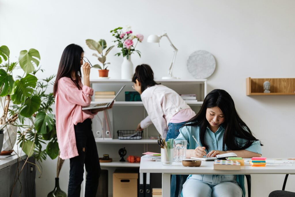 Three women working together in a modern office with plants and bookshelves.